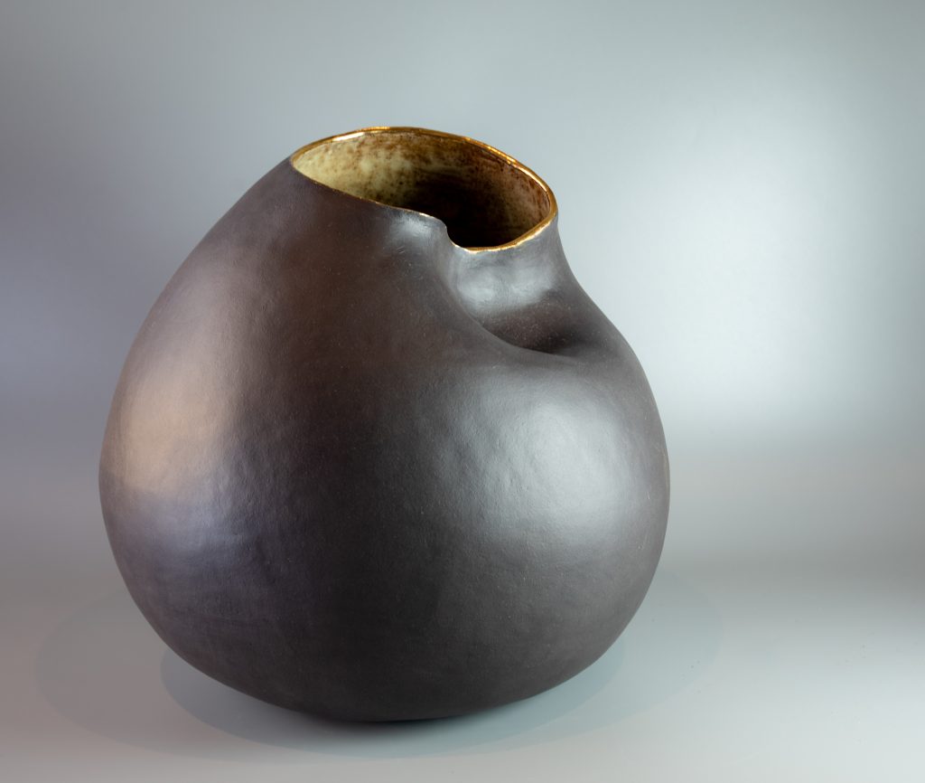 Large sculptural black clay vessel with rounded form, indented surface and irregular opening