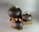 Three rounded black clay vessels with flared glazed necks displayed on wooden blocks