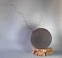 Circular black clay sculptural vessel with branching metal stems on a wooden base