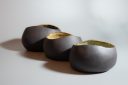 Three hand-built black clay bowls with asymmetrical openings and glazed interiors